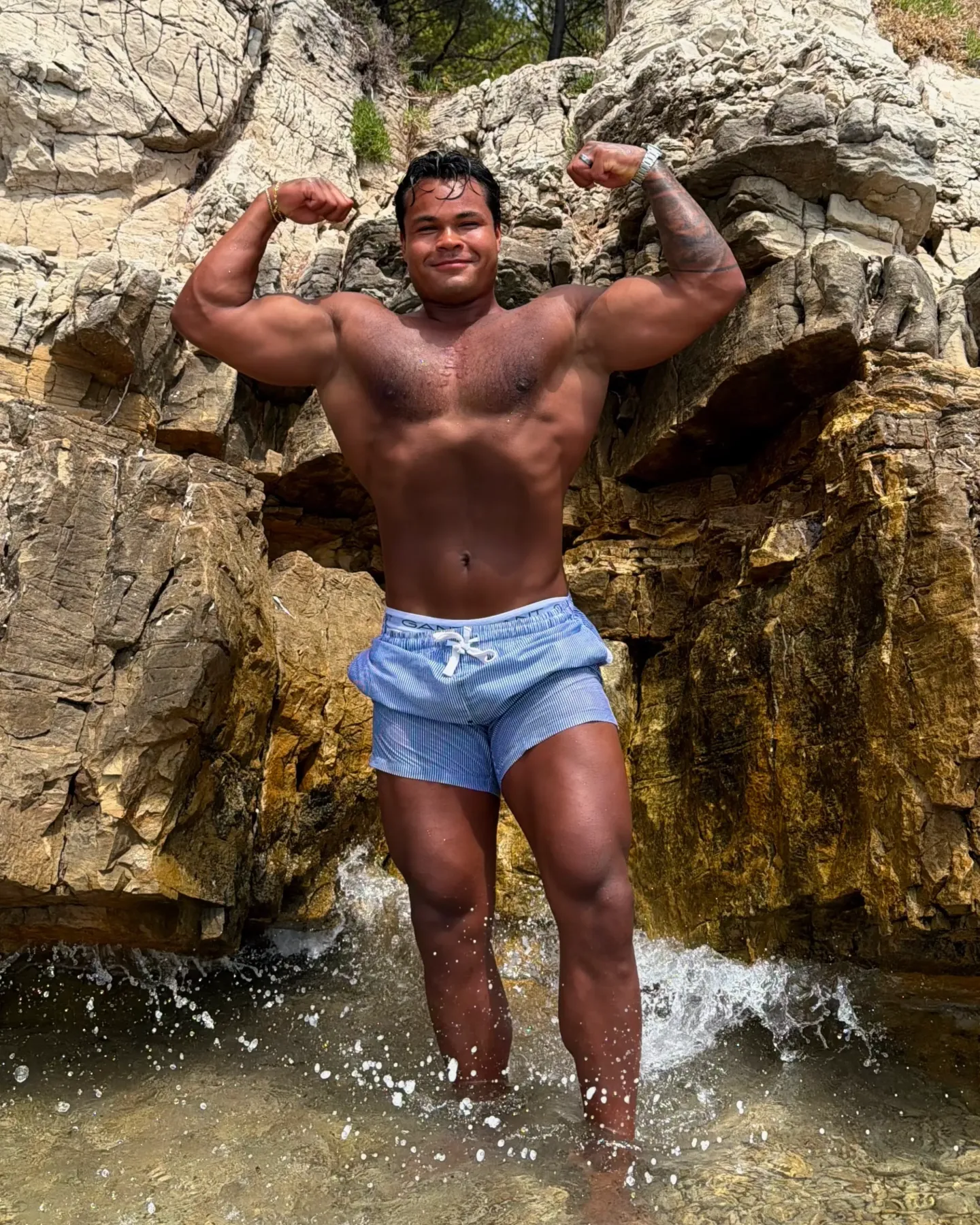 Coachen viser biceps i vannet foran en klippevegg.